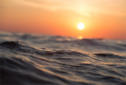 Sun setting over the ocean; closeup of small waves with sun in background